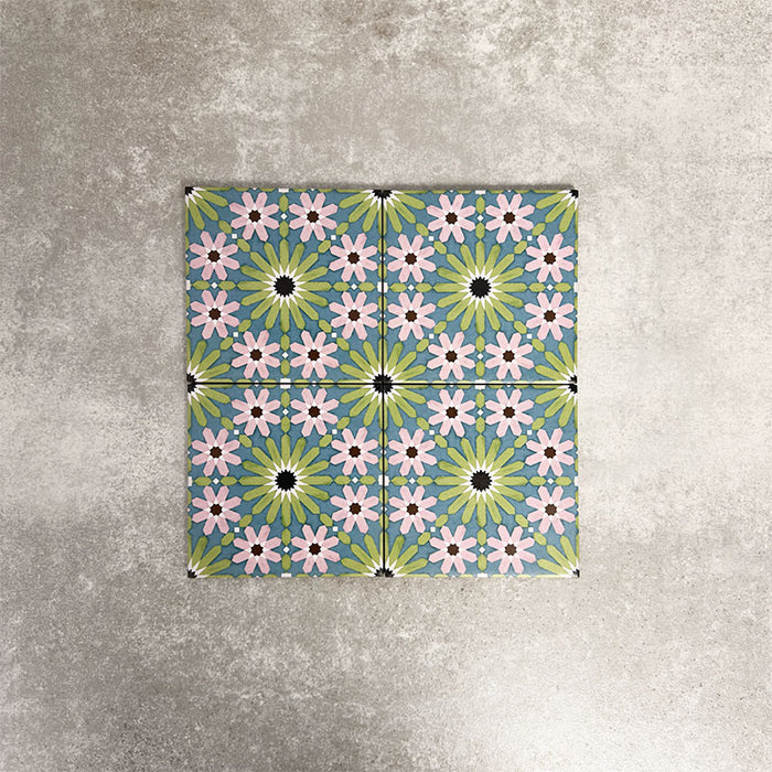 Fez Mini Summer 15x15cm Moroccan-style porcelain tile displayed against a textured grey background, highlighting the colourful geometric star pattern in soft green, blue and blush pink tones with an encaustic-inspired finish.