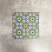 Fez Mini Summer 15x15cm Moroccan-style porcelain tile displayed against a textured grey background, highlighting the colourful geometric star pattern in soft green, blue and blush pink tones with an encaustic-inspired finish.