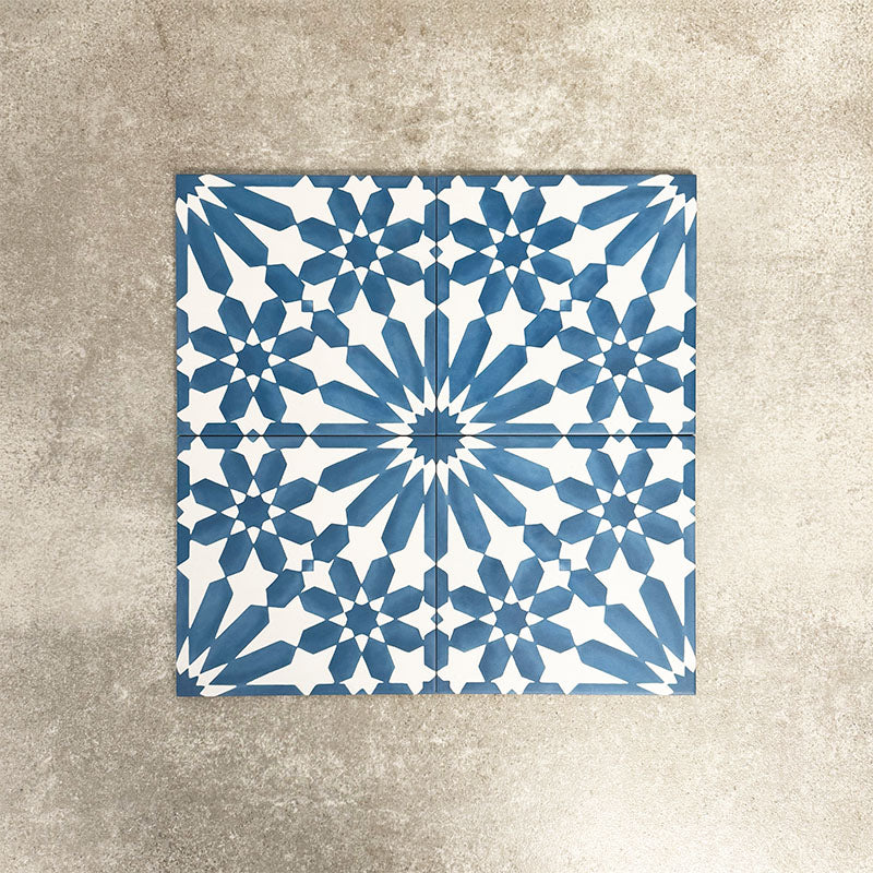 Fez Azure Blue 20x20cm Moroccan-style porcelain tiles arranged as a four-tile panel, highlighting the crisp blue and white geometric star pattern and the full repeat design against a textured grey background.