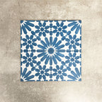 Fez Azure Blue 20x20cm Moroccan-style porcelain tiles arranged as a four-tile panel, highlighting the crisp blue and white geometric star pattern and the full repeat design against a textured grey background.