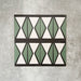 Abstract Hourglass Patterned Tiles in a 20x20cm format, displayed in a repeated grid layout to showcase the bold geometric hourglass design. Muted green and soft cream tones are framed with charcoal detailing, creating a clean, contemporary pattern ideal for feature walls, floors or decorative splashbacks.