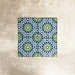 Fez Mini Springs 15x15cm Moroccan-style porcelain tiles arranged as a four-tile panel, highlighting the full repeat design with layered blue and soft green geometric star motifs against a textured grey background.