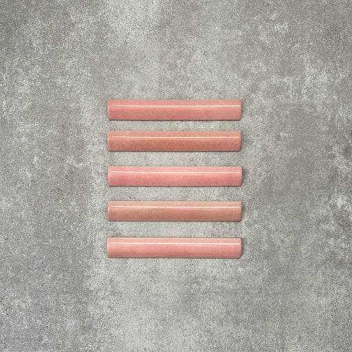 Flat lay of Zellige Rose Pink Bullnose 3 × 20cm Moroccan-style ceramic trim tiles in soft blush and dusty pink tones, shown with a smooth rounded edge and subtle glaze variation, arranged on a textured grey background to highlight the handcrafted zellige-effect finish and decorative edging profile.