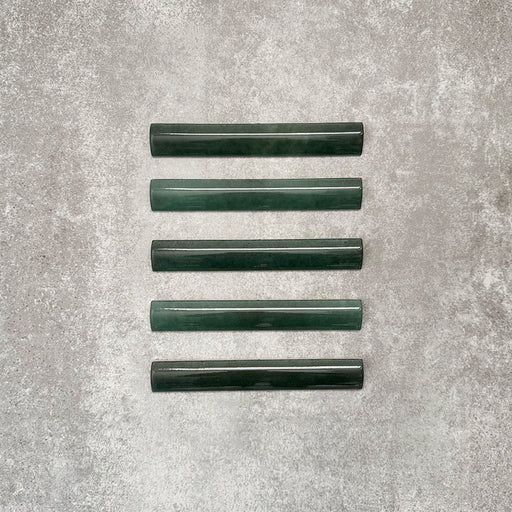 Flat lay of Zellige Royal Green Bullnose 3 × 20cm Moroccan-style ceramic trim tiles in rich deep green tones, displayed with a smooth rounded edge and glossy glaze, arranged on a textured grey background to highlight the handcrafted zellige-effect finish and decorative edging profile.