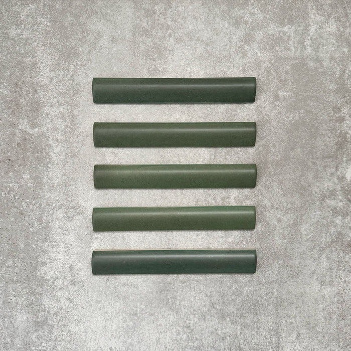 Flat lay of Zellige Malachite Green 3×20cm Moroccan-style ceramic bullnose tiles, showcasing the rounded edge profile, rich green glaze and subtle tonal variation on a neutral background.