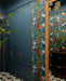 Hallway interior featuring Abstract Compass Green 20x20cm patterned floor tiles in green, white and red tones, styled with teal panelling, botanical wallpaper, wooden console table, and decorative accessories in a characterful entrance space.