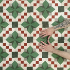 Close-up of Abstract Compass Green 20x20cm patterned tiles arranged to showcase the repeating geometric design in green, white and red tones, with hands demonstrating tile placement and alignment.