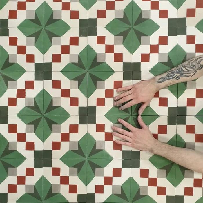 Close-up of Abstract Compass Green 20x20cm patterned tiles arranged to showcase the repeating geometric design in green, white and red tones, with hands demonstrating tile placement and alignment.