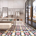 Retail interior featuring Abstract Contori Patterned Tiles in a 20x20cm format, laid as a decorative floor design. The elegant geometric pattern blends soft blush pink, muted green, mustard yellow and charcoal tones, paired with marble counters, neutral furnishings and contemporary lighting to create a refined, high-end boutique setting.