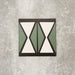 Single Abstract Hourglass Patterned Tile in a 20x20cm format, featuring a bold geometric hourglass design in muted green and soft cream tones with charcoal detailing. A contemporary patterned tile ideal for feature walls, floors or statement splashbacks.