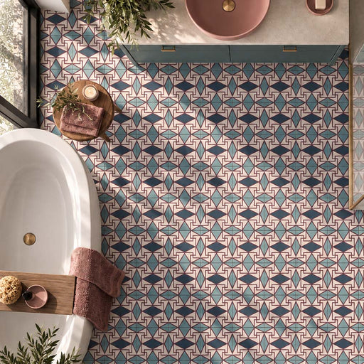 Overhead view of a bathroom featuring Abstract Iris 20cm x 20cm patterned floor tiles, showcasing a bold geometric design in turquoise, deep blue, burgundy and cream tones, paired with a white freestanding bath and coordinating pink and blue accents.
