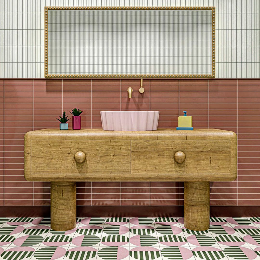 Bathroom interior featuring Abstract Serit Patterned Tiles in a 20x20cm format, laid as a bold geometric floor design. The repeating pattern combines soft pink, deep green and crisp white tones with striped detailing, paired with a wooden vanity unit and blush basin to create a playful yet contemporary bathroom setting.