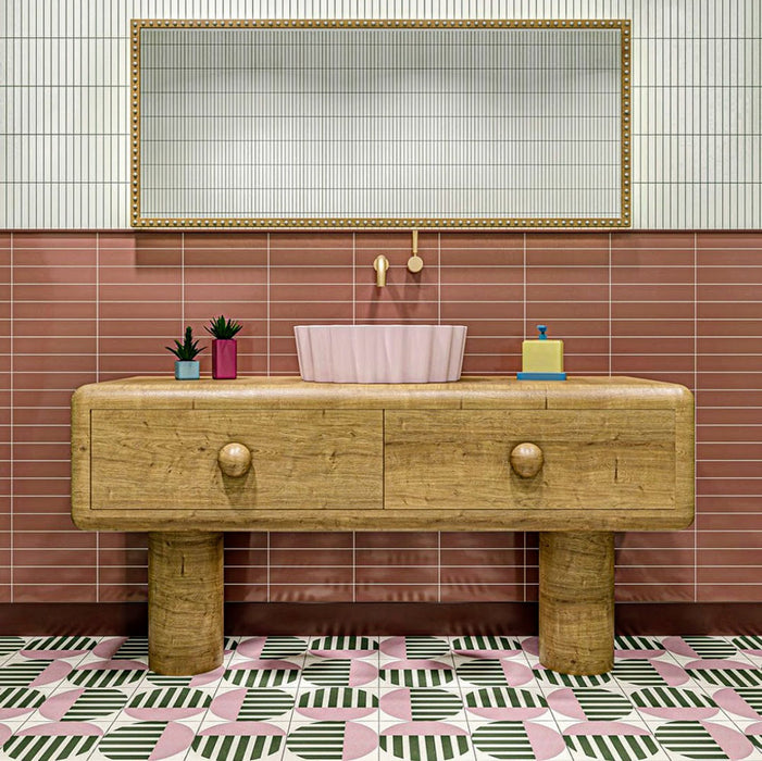 Bathroom interior featuring Abstract Serit Patterned Tiles in a 20x20cm format, laid as a bold geometric floor design. The repeating pattern combines soft pink, deep green and crisp white tones with striped detailing, paired with a wooden vanity unit and blush basin to create a playful yet contemporary bathroom setting.