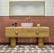 Bathroom interior featuring Abstract Serit Patterned Tiles in a 20x20cm format, laid as a bold geometric floor design. The repeating pattern combines soft pink, deep green and crisp white tones with striped detailing, paired with a wooden vanity unit and blush basin to create a playful yet contemporary bathroom setting.