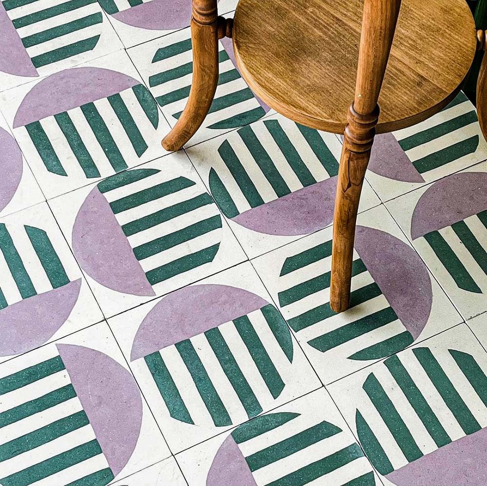 Abstract Serit Patterned Tiles in a 20x20cm format, laid as a bold geometric floor design featuring soft pink semicircles and deep green striped detailing on a crisp white background. Styled with a wooden chair to highlight the repeating pattern and showcase the tiles in a contemporary interior setting suitable for floors.