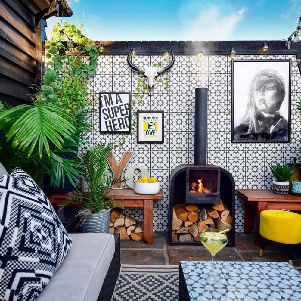 Outdoor seating area featuring Agadir Black & White Moroccan-style 20x20cm porcelain tiles used as a feature wall, showcasing a bold geometric star pattern, styled with a wood-burning stove, plants and eclectic outdoor furniture.