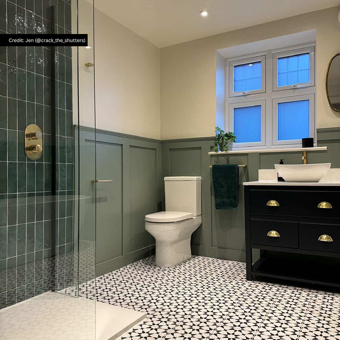 Bathroom interior featuring Agadir Black & White 20x20cm Moroccan style patterned porcelain floor tiles in a geometric black and white design, styled with green wall panelling, brass fixtures and a modern vanity unit.