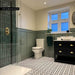 Bathroom interior featuring Agadir Black & White 20x20cm Moroccan style patterned porcelain floor tiles in a geometric black and white design, styled with green wall panelling, brass fixtures and a modern vanity unit.