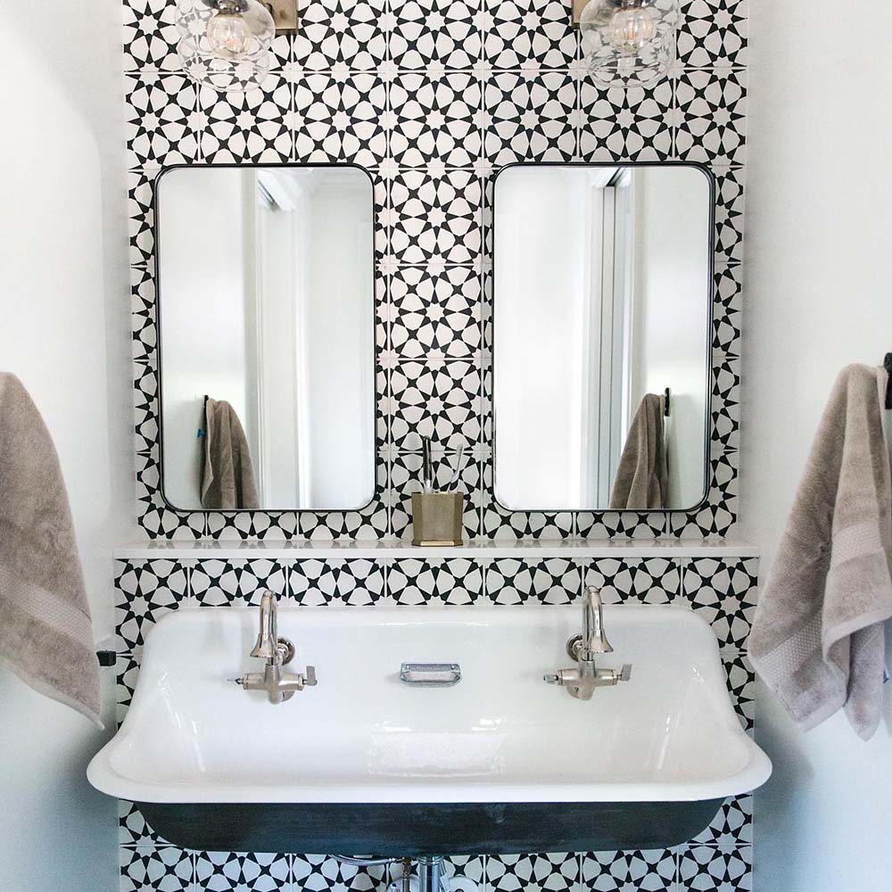 Bathroom sink area featuring Agadir Black & White Mini Moroccan-style 15x15cm porcelain wall tiles, showcasing a bold geometric star pattern, styled with twin mirrors, a classic basin and chrome taps.