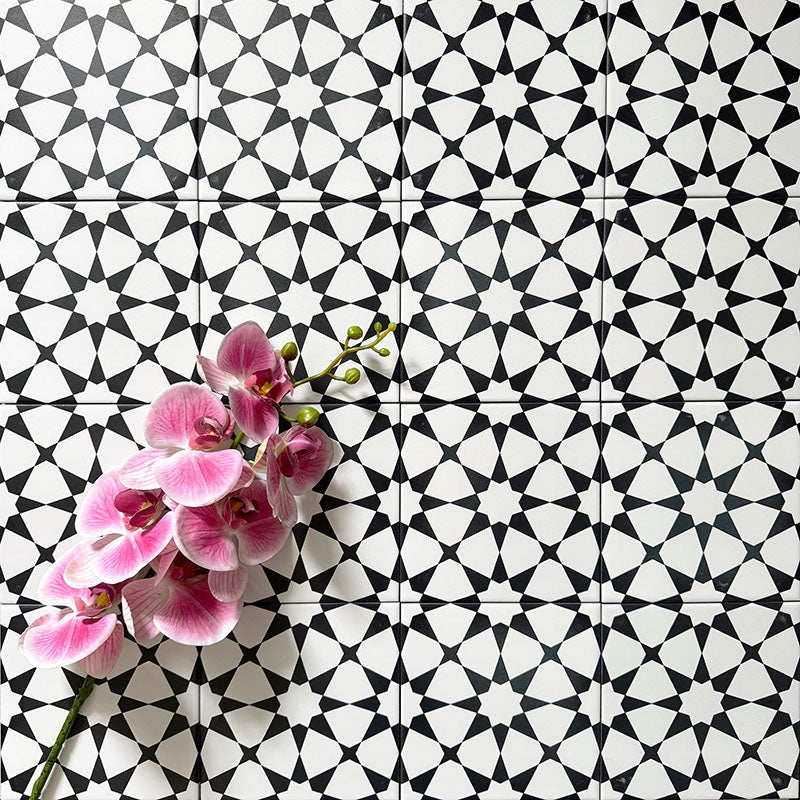 Agadir Black & White Mini Moroccan-style 15x15cm porcelain floor tiles laid in a repeating geometric star pattern, styled with a decorative orchid to highlight the bold black and white design.