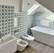 Bathroom interior featuring Agadir Green Moroccan-style 20x20cm porcelain wall tiles, showcasing a repeating geometric star pattern in green and white, styled with a freestanding bath, modern sanitaryware and a bright, airy layout.