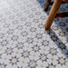 Marketing image of Agadir Natural Moroccan-style 20x20cm porcelain tiles laid on a floor, featuring a soft neutral geometric star pattern with subtle grey and warm beige tones, styled with a wooden chair for a lived-in look.