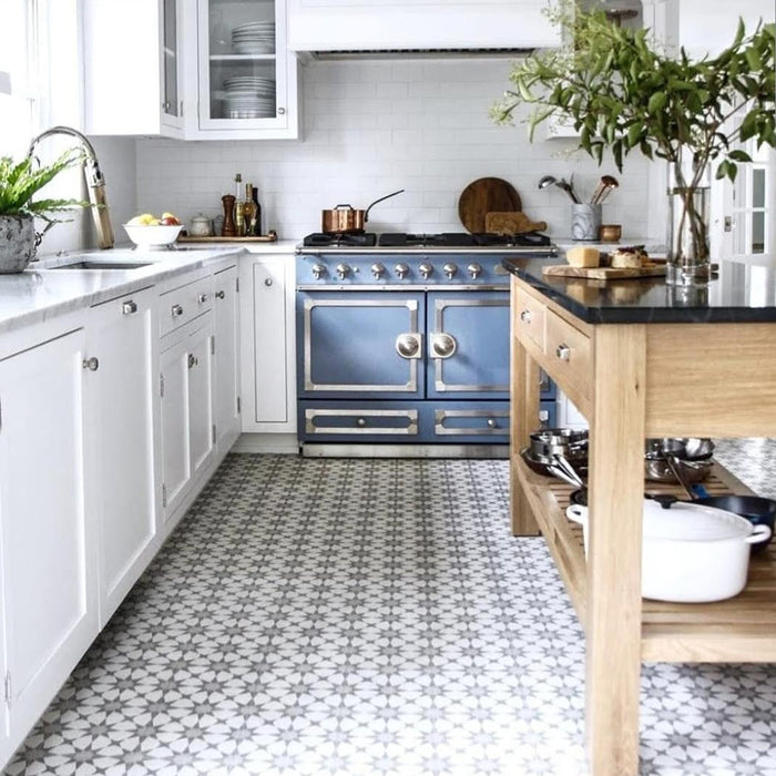 Kitchen interior featuring Agadir Silver Moroccan-style 20x20cm porcelain floor tiles, showcasing a soft geometric star pattern in silver and white beneath white cabinetry and a wooden island.