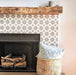 Agadir Silver Moroccan-style 20x20cm porcelain tiles used to frame a fireplace, featuring a soft grey geometric pattern paired with a rustic wooden mantel and neutral accessories for a warm, contemporary living space.