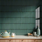 Interior wall featuring Alchemy Hunter Green 6.5cm x 30cm tiles laid vertically, showcasing rich green tones and subtle surface variation, styled with decorative ceramics and a light wood cabinet.