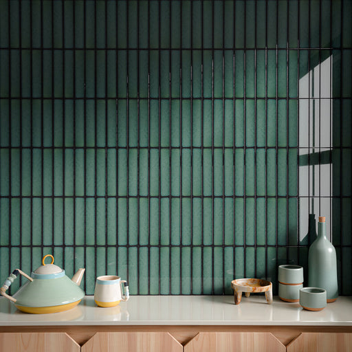Interior wall featuring Alchemy Hunter Green 6.5cm x 30cm tiles laid vertically, showcasing rich green tones and subtle surface variation, styled with decorative ceramics and a light wood cabinet.