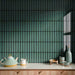 Interior wall featuring Alchemy Hunter Green 6.5cm x 30cm tiles laid vertically, showcasing rich green tones and subtle surface variation, styled with decorative ceramics and a light wood cabinet.
