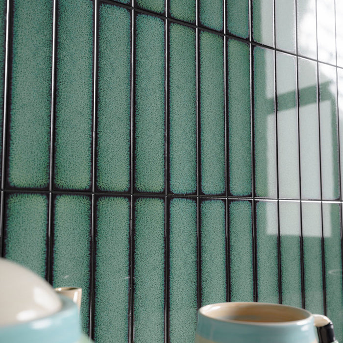 Close-up of Alchemy Hunter Green 6.5cm x 30cm wall tiles laid vertically, highlighting the rich green glaze, dark edging and distinctive speckled surface variation with a glossy finish.