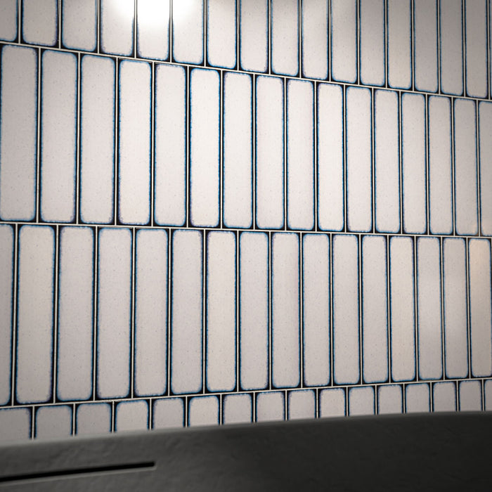 Close-up of Alchemy Magma White 6.5cm x 30cm wall tiles laid vertically, highlighting the soft white surface, rounded edges and distinctive dark blue edging.