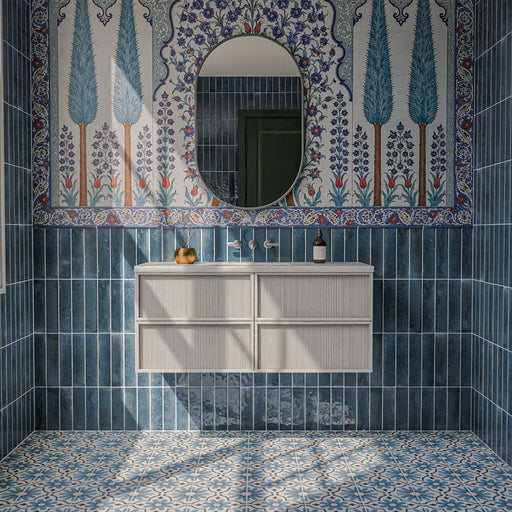 Allegra Blue 6cm x 25cm gloss brick wall tiles, featuring rich blue tonal variation throughout a statement bathroom, paired with intricate blue patterned floor tiles and a decorative floral mural.