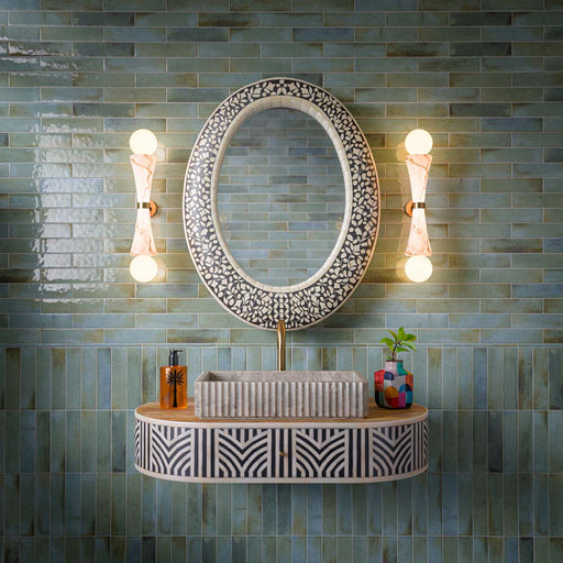 Bathroom featuring Allegra Celadon Green gloss brick tiles, combining soft green and blue-toned marble-effect variation with a reflective glazed finish. Installed in both horizontal and vertical layouts, the tiles create subtle contrast and visual interest, while the decorative vanity, statement mirror and warm brass accents bring a sophisticated Mediterranean-inspired character to the space.