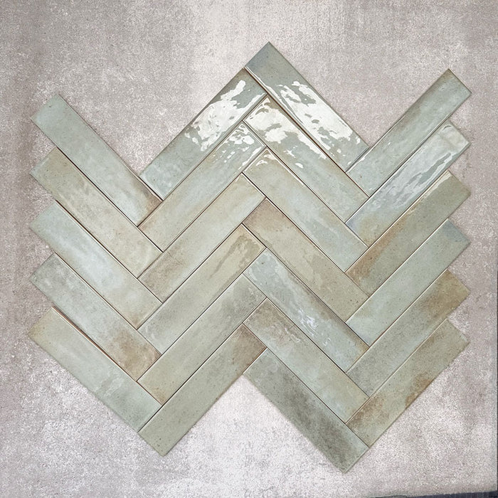 Allegra Celadon Green Gloss Brick ceramic tiles in a 6 × 25cm format, arranged in a herringbone pattern to showcase the soft green tones, glossy finish and subtle handmade-style variation.
