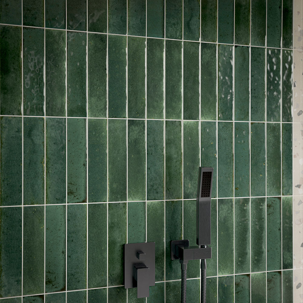 Close-up of Allegra Green 6cm x 25cm gloss brick tiles in a shower, showcasing rich green tonal variation and a glossy finish, paired with contemporary matt black shower fixtures.