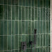 Close-up of Allegra Green 6cm x 25cm gloss brick tiles in a shower, showcasing rich green tonal variation and a glossy finish, paired with contemporary matt black shower fixtures.