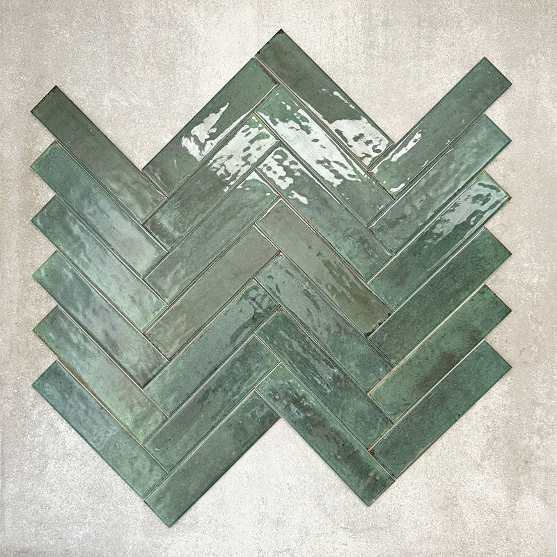 Allegra Green Gloss Brick ceramic tiles in a 6 × 25cm format, arranged in a herringbone pattern to showcase the deep green colour, high-gloss finish and subtle handmade-style surface variation.