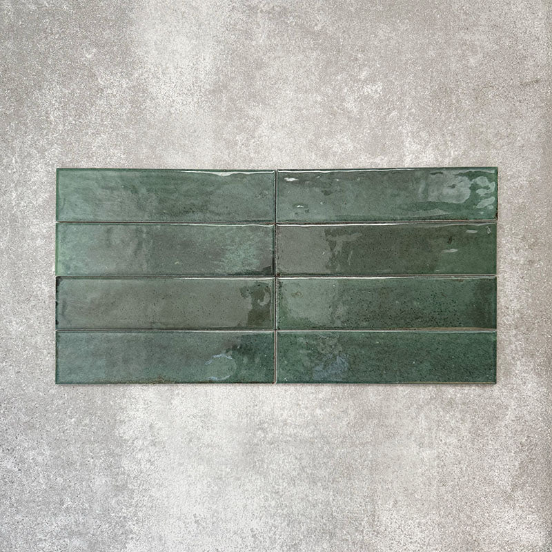 Allegra Green Gloss Brick ceramic tiles in a 6 × 25cm format, laid horizontally to highlight the deep green colour, glossy finish and subtle tonal and surface variation.