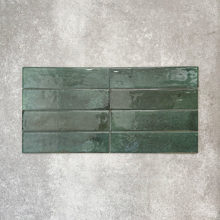 Allegra Green Gloss Brick ceramic tiles in a 6 × 25cm format, laid horizontally to highlight the deep green colour, glossy finish and subtle tonal and surface variation.