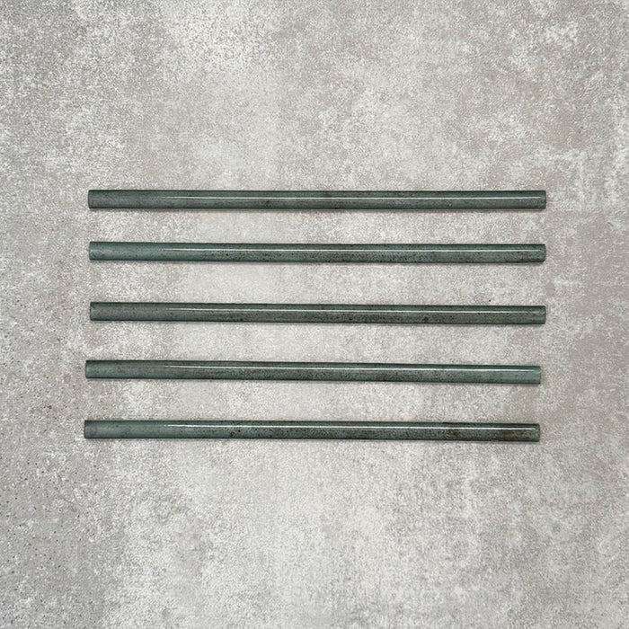 Allegra Green Gloss pencil bullnose border tiles in a 1.2 × 30cm ceramic format, shown as five pieces laid horizontally to display the slim profile, rounded edges, tonal green variation and glossy glazed finish on a neutral textured background.