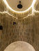 Curved shower enclosure lined with Allegra Sage Green gloss brick tiles in a vertical layout, highlighting a high-shine glazed finish with natural tonal variation, complemented by a black rainfall shower and soft integrated ceiling lighting.