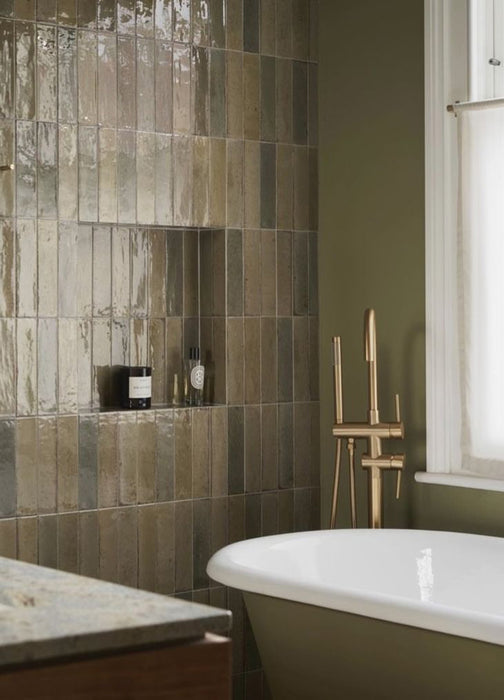 Bathroom feature wall finished with Allegra Sage Green gloss brick tiles in a vertical stack layout, showcasing rich sage and olive tones with natural surface variation, paired with a freestanding bath, brushed brass tapware and a soft green painted wall.