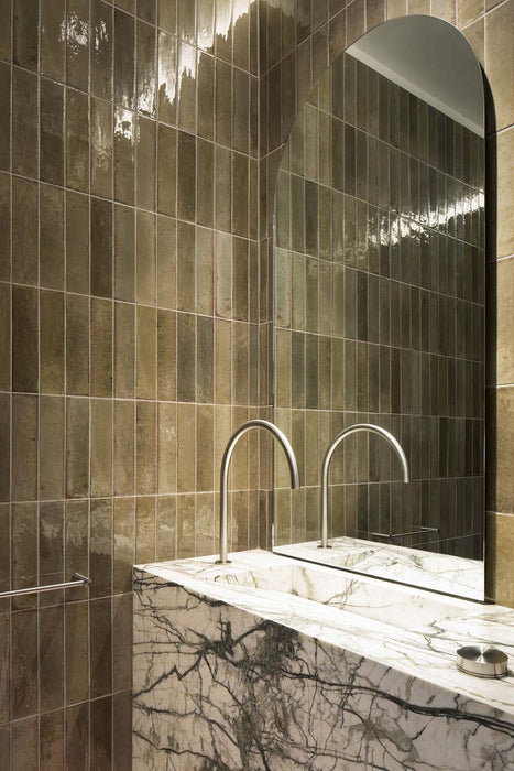 Bathroom wall finished with Allegra Sage Green gloss brick tiles in a vertical layout, featuring subtle tonal variation and a reflective glazed surface, paired with a marble vanity, wall-mounted basin and contemporary chrome tapware.
