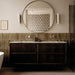 Allegra Sage Green 6x25cm gloss brick tiles installed as a bathroom feature wall, showcasing soft earthy green tones with gentle shade variation and a reflective glazed finish. The elongated format adds subtle texture and depth, complementing dark wood cabinetry, marble surfaces and warm brass accents for a refined, contemporary look.