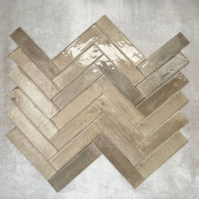 Allegra Sage Green Gloss Brick ceramic tiles in a 6 × 25cm format, arranged in a herringbone pattern to showcase the muted green tones, glossy finish and subtle handmade-style variation.