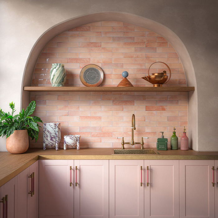 Kitchen featuring Allegra Tusk Pink gloss brick tiles in a warm blush-pink marble effect, creating a soft and inviting splashback within an arched alcove. Paired with pale pink cabinetry, natural wood surfaces and brass fixtures, the design blends contemporary elegance with Mediterranean-inspired warmth, bringing colour, texture and character to the space.