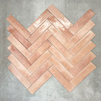 Allegra Tusk Pink Gloss Brick ceramic tiles in a 6 × 25cm format, arranged in a herringbone pattern to showcase the soft pink tones, glossy finish and subtle handmade-style variation.