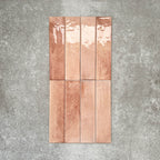 Allegra Tusk Pink Gloss Brick ceramic tiles in a 6 × 25cm format, shown laid vertically to highlight the soft pink tones, glossy finish and subtle handmade-style variation.
